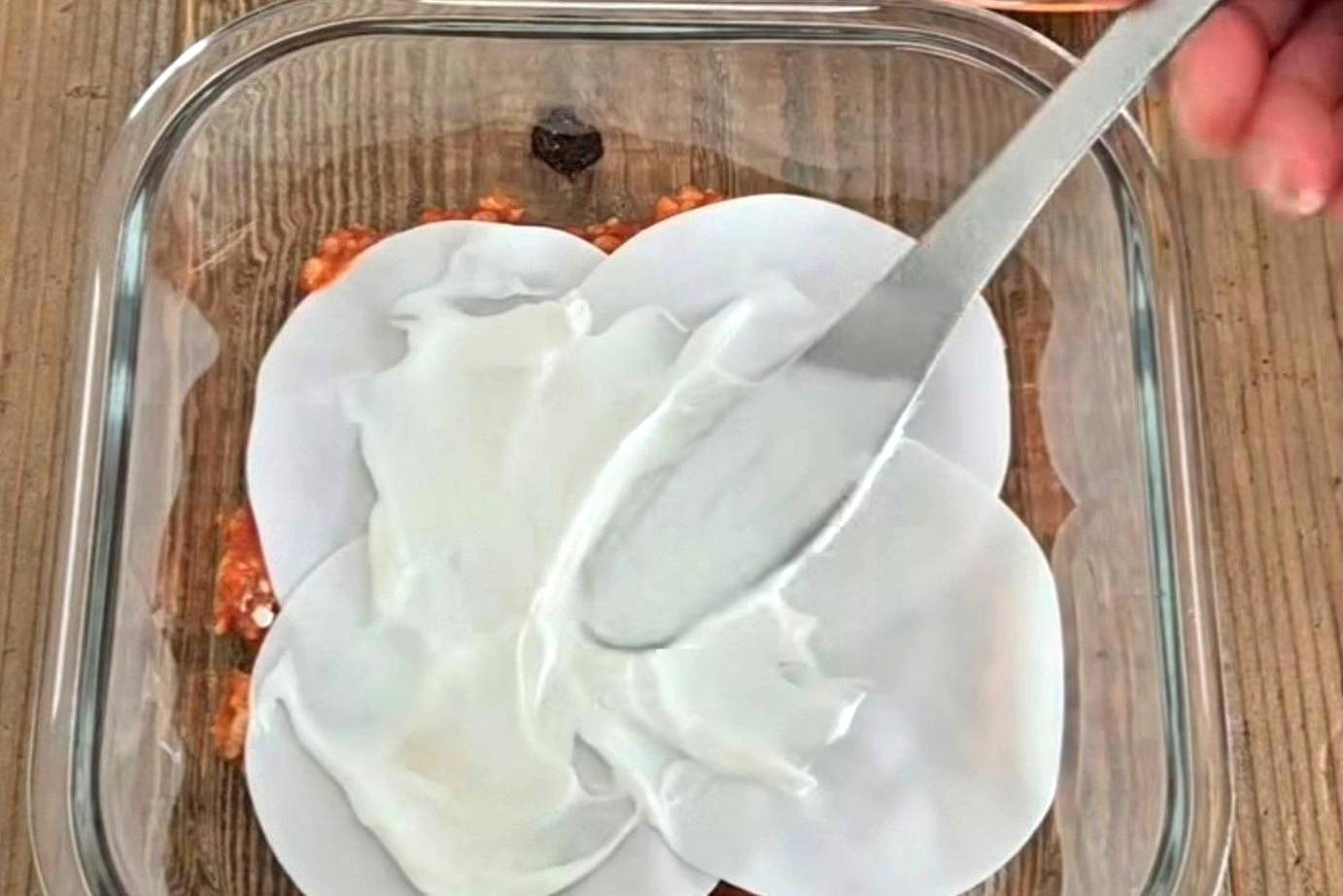 ミートソースの上に餃子の皮、ヨーグルトを塗っている